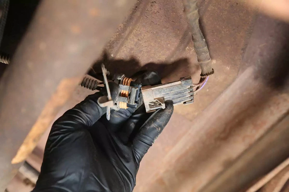 A mechanic removing the oxygen sensor plug from the vehicle’s wiring harness.