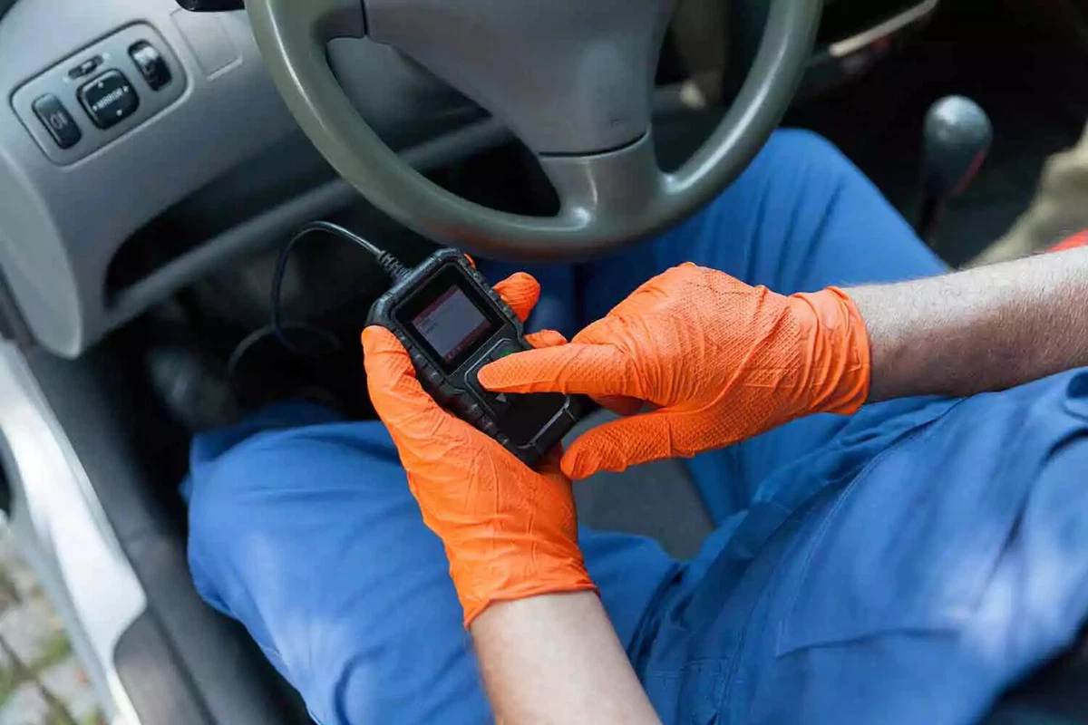 A mechanic wearing orange protective gloves using an OBDII reader to identify the cause of the check engine light code.