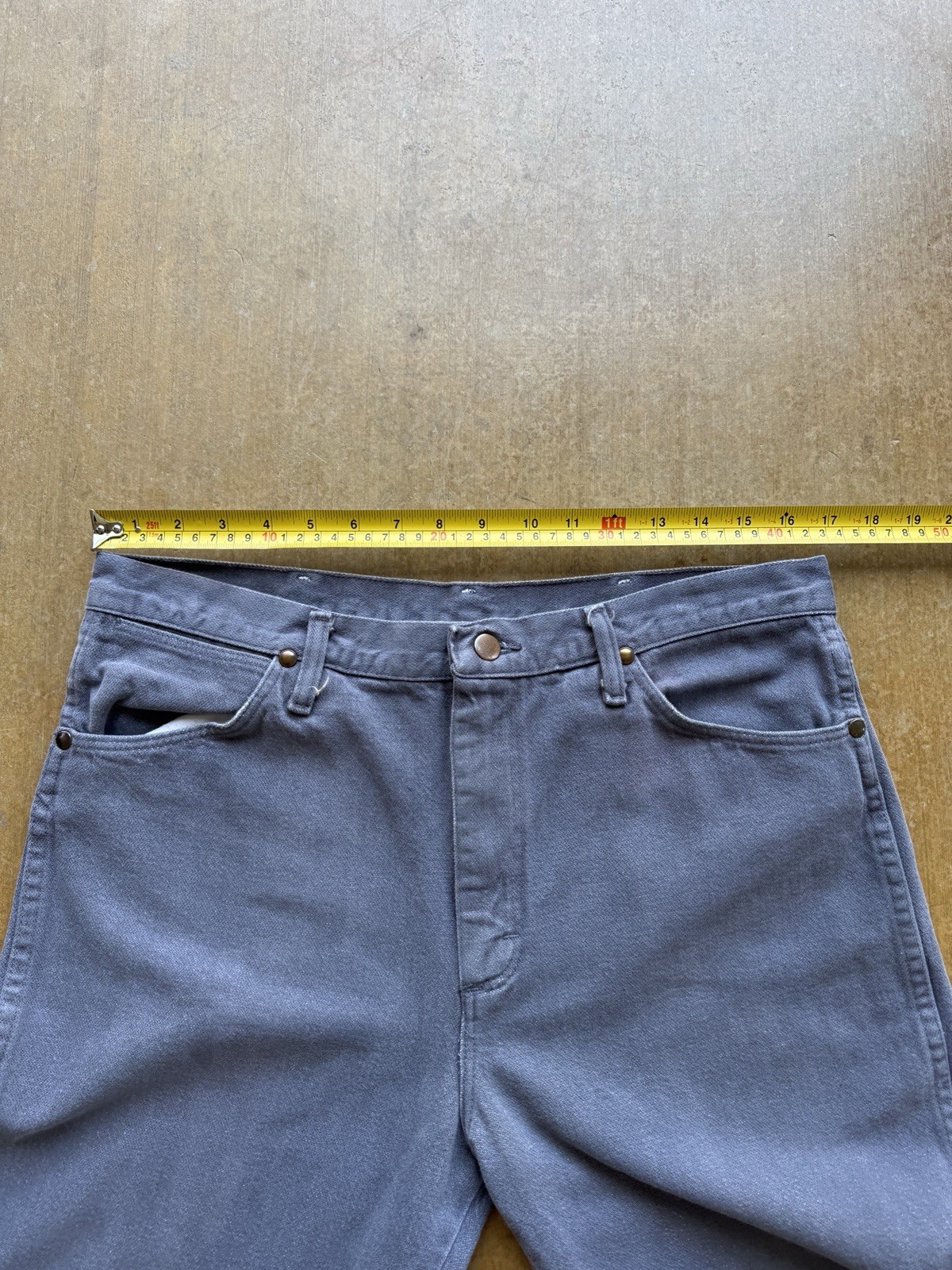 Gray VTG 90s Wrangler straight leg cowboy pants with five pockets, button closure, and yellow measuring tape across the waistband.
