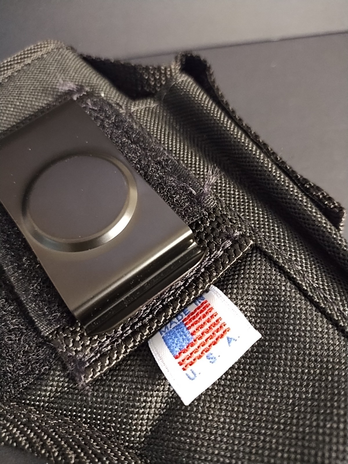 Black nylon IWB holster with metal clasp, two front pockets, and white USA flag patch on black fabric background.