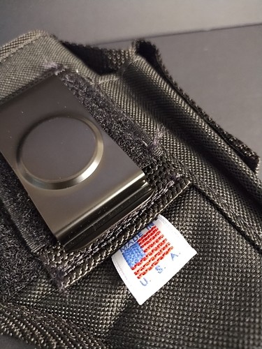 Black nylon IWB holster with metal clasp, two front pockets, and white USA flag patch on black fabric background.