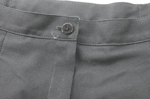 Black Jantzen women’s pants with front button closure, pleated detailing, and two front slash pockets on a dark fabric background.