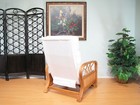 White rattan recliner chair with padded backrest and armrests, placed on a light wood floor near a wall painting.