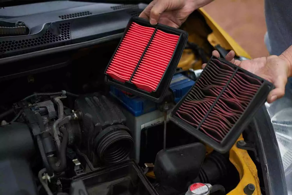 A mechanic holds two red engine air filters. The filter on the left is clean. The filter on the right is extremely dirty.