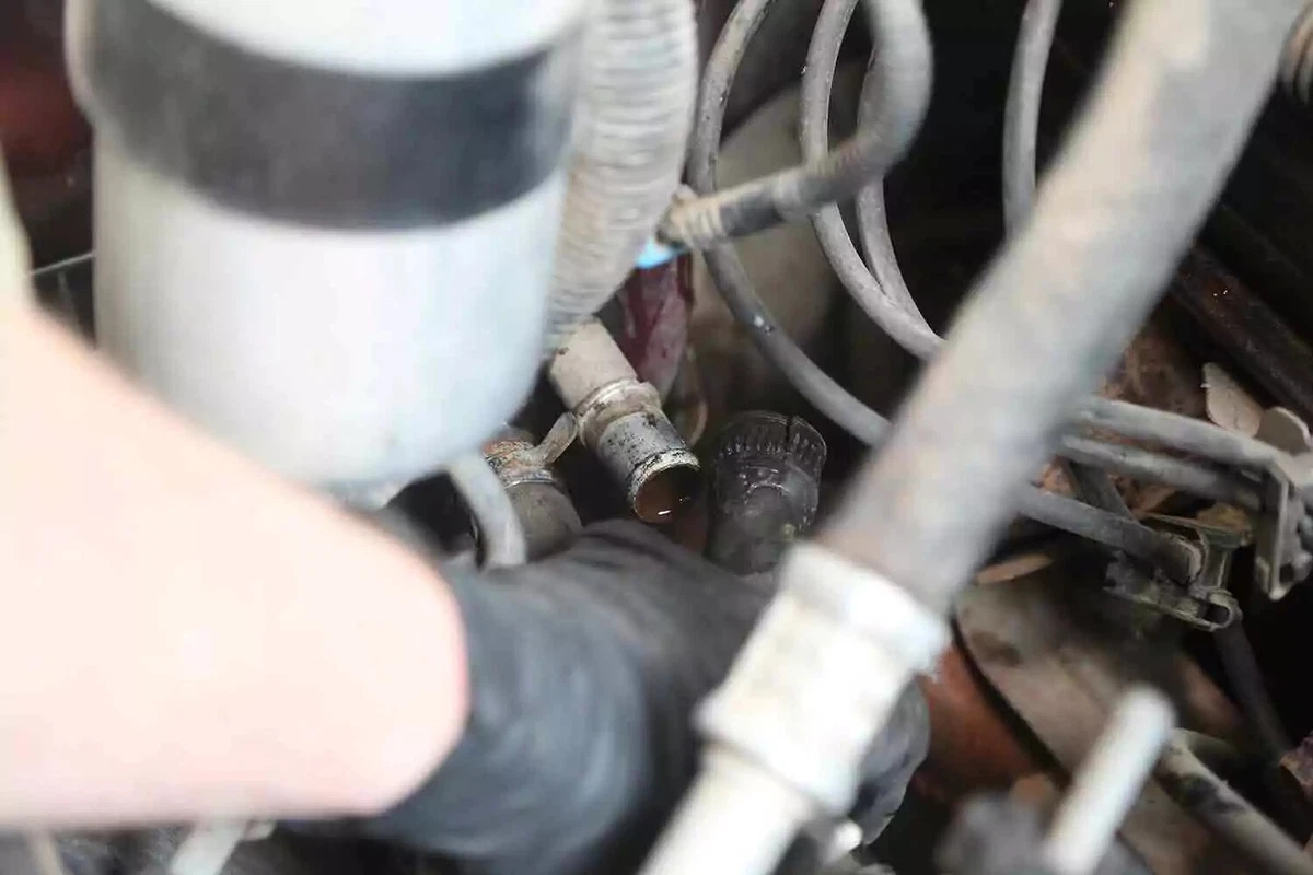 A mechanic wearing black gloves removes the hose from a heater core pipe.