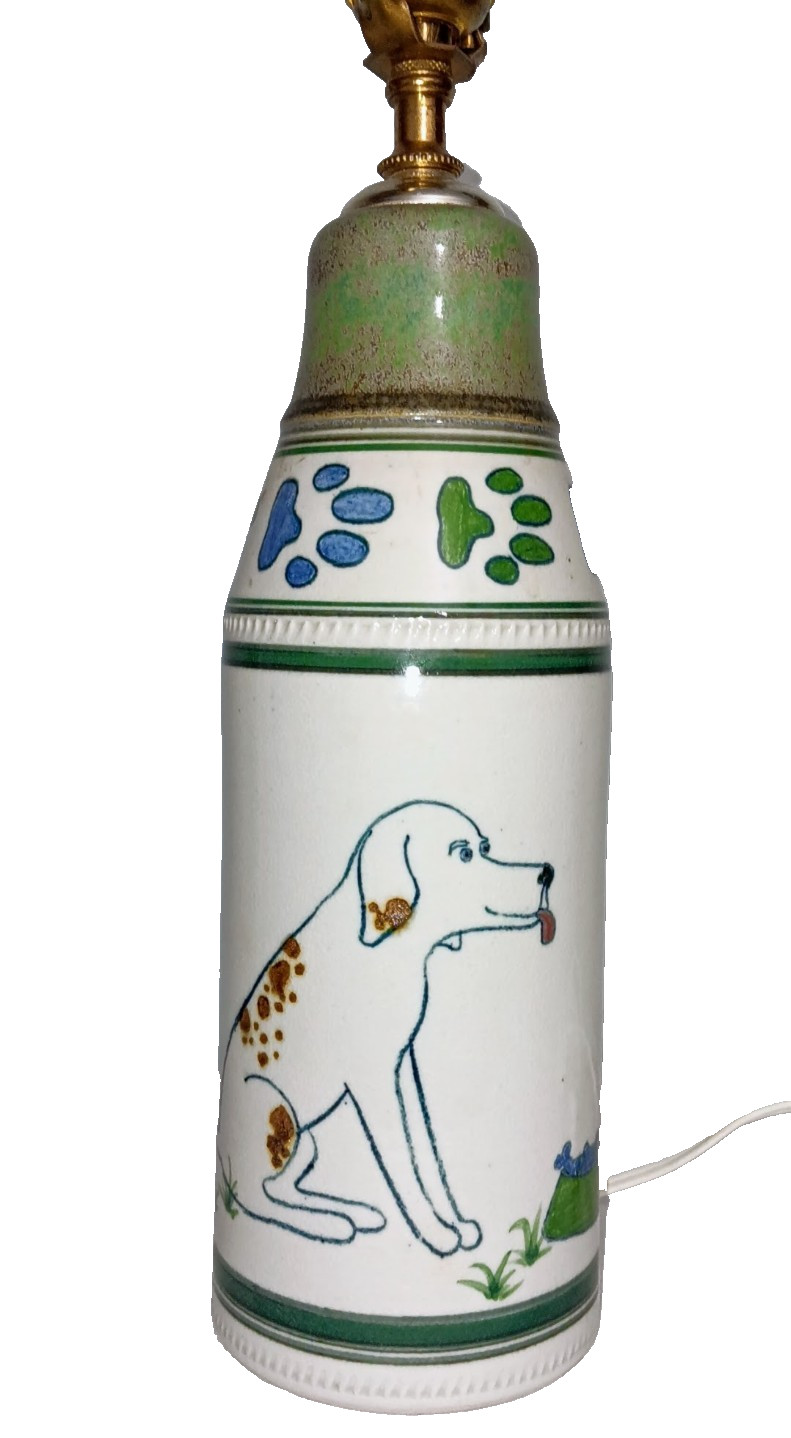 Cream ceramic table lamp base hand-painted with a brown and blue dog design and a sage-green cap, shown cut out on white, no shade.