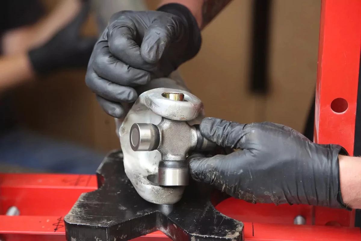 A mechanic wearing black gloves slides the joint cross into the press.