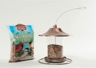 Clear plastic bag of 53002 Farmer’s Delight Wild Bird Food with cherry flavor, copper bird feeder, and two birds.