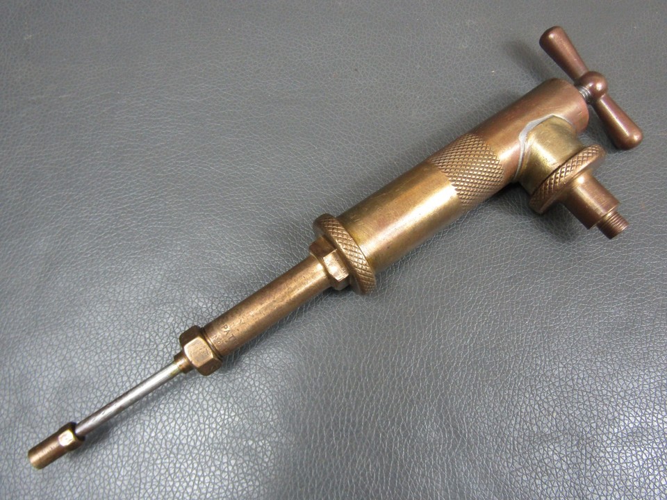 A chunky pre-WWII brass grease gun that looks like a steampunk artifact — actual industrial history you can hold in your hand.