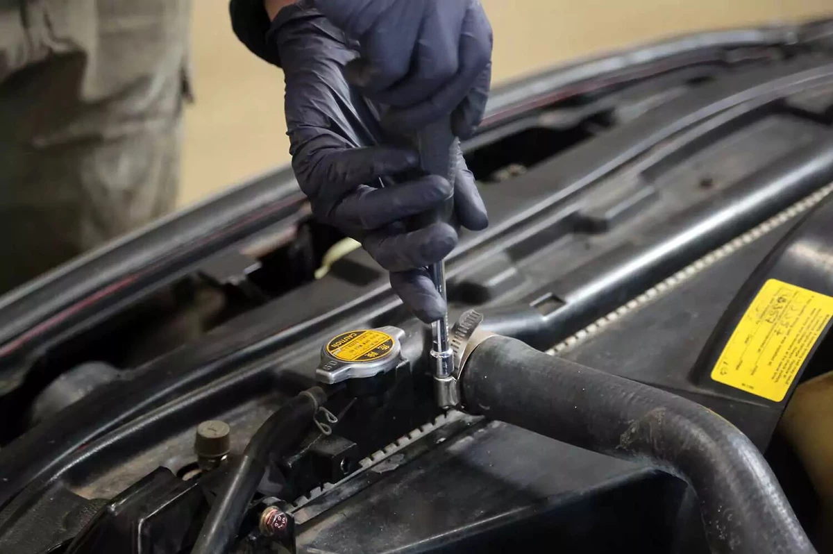 Loosening the upper radiator hose clamp with a socket driver.