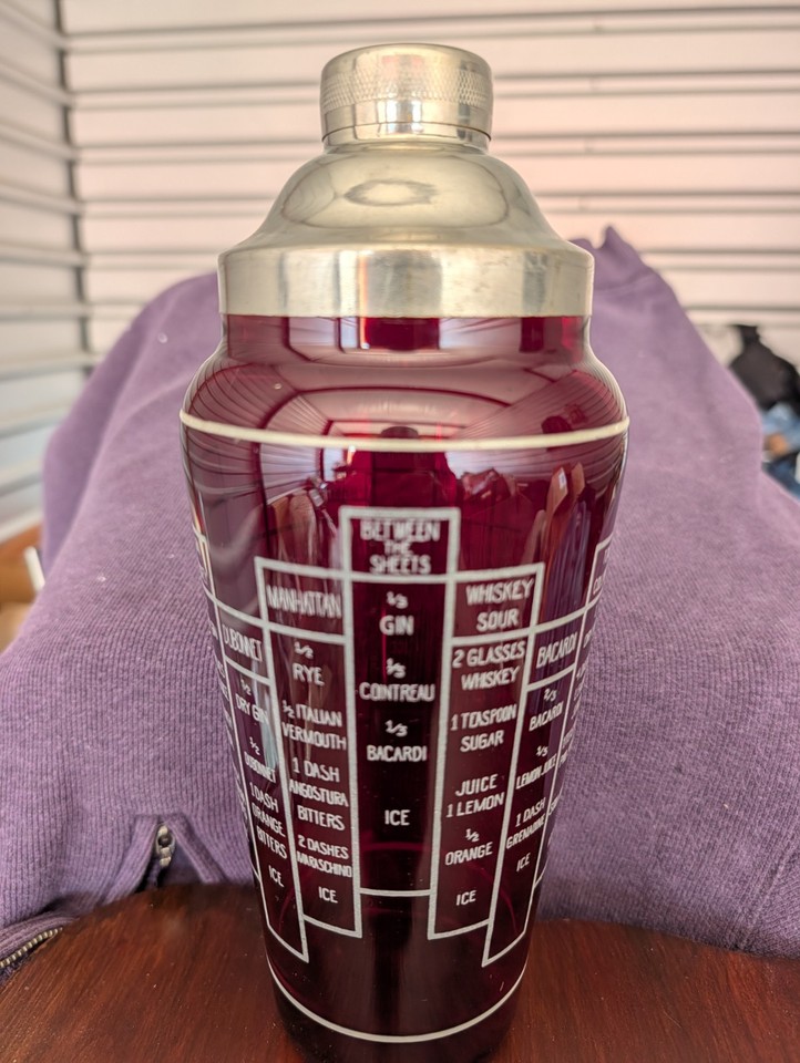 A tall 1930s dark ruby red cocktail shaker with 16 embossed recipes right on the glass — Prohibition-era glamour meets functional party prop.