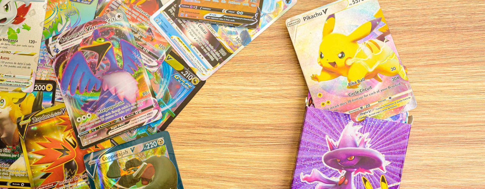 Auf einem Holztisch liegt eine Sammlung glänzender Pokémon-Karten, darunter eine Pikachu V-Karte und weitere farbenfrohe, holografische Karten.