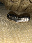 Gold brooch with embedded text “PRICELESS” in black, slightly tarnished gold tone on textured surface.