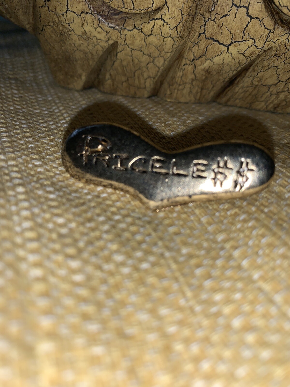 Gold brooch with embedded text “PRICELESS” in black, slightly tarnished gold tone on textured surface.