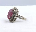 Silver ring with large oval red gemstone center, surrounded by small clear diamonds in a polished band.