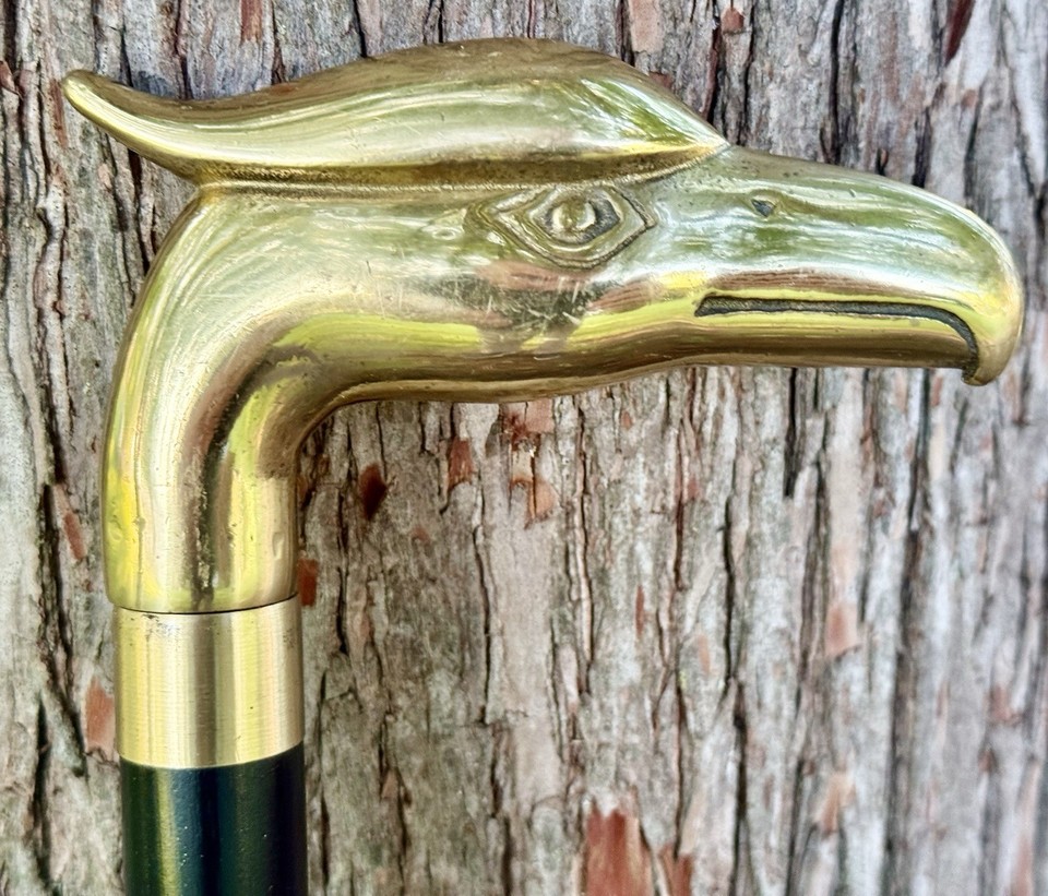 A full-sized solid brass eagle-head walking cane on a hardwood shaft — the kind of artifact that looks like it belongs in a Victorian gentleman's study and demands to be picked up.