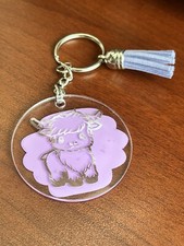 Baby Highland Cow acrylic keychain with tassel. Set on a Purple background.