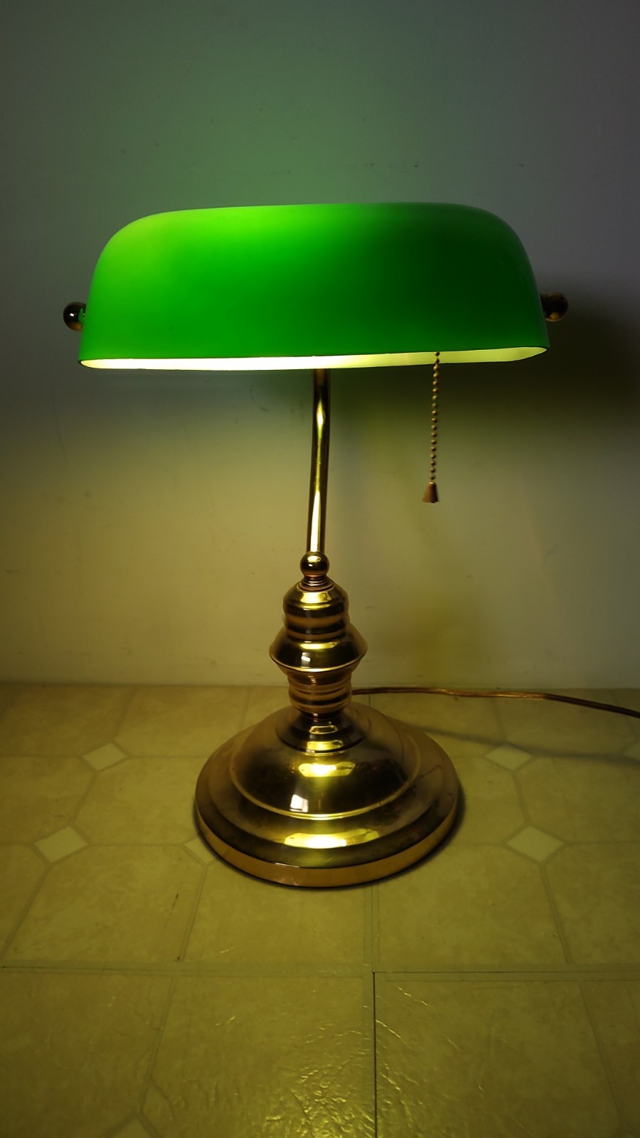 Brass banker's desk lamp with a green glass shade and pull chain.
