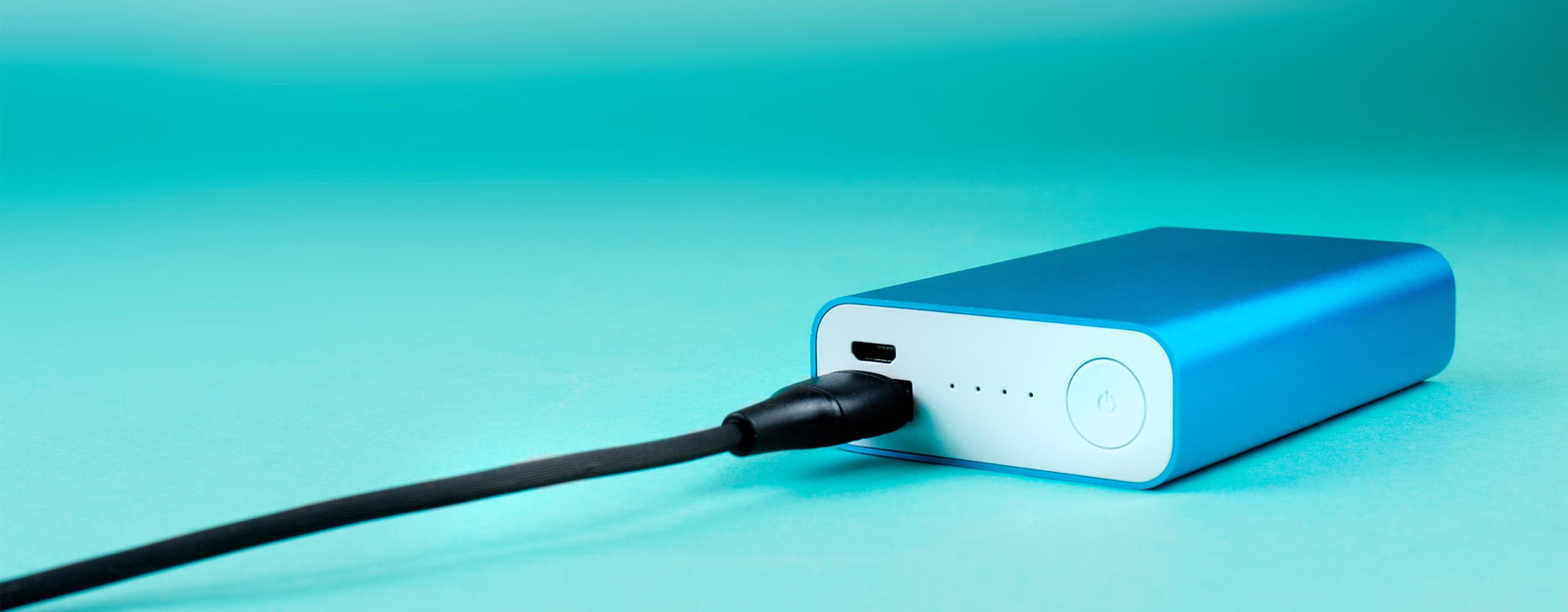 Eine blaue Powerbank mit einem schwarzen Ladekabel liegt auf einem türkisen Untergrund.