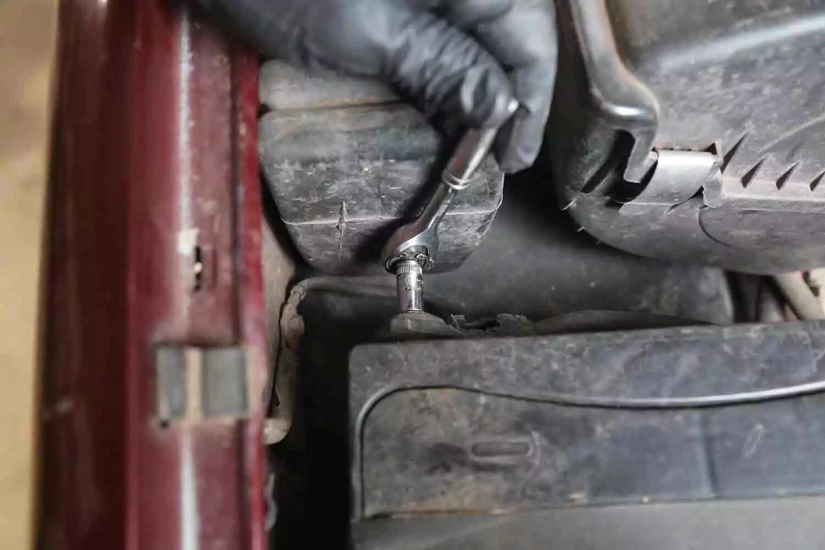 A mechanic wearing a black glove disconnects the negative battery terminal.