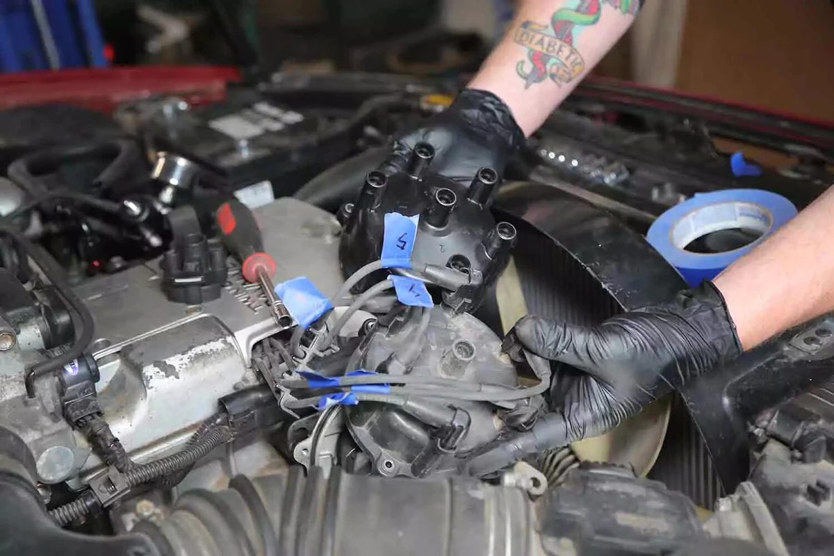 A mechanic wearing black gloves compares a new distributor cap to the old one.