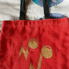 Rote Stoff-Tragetasche mit schwarzen Henkeln,  gelb-goldenem Notenaufdruck