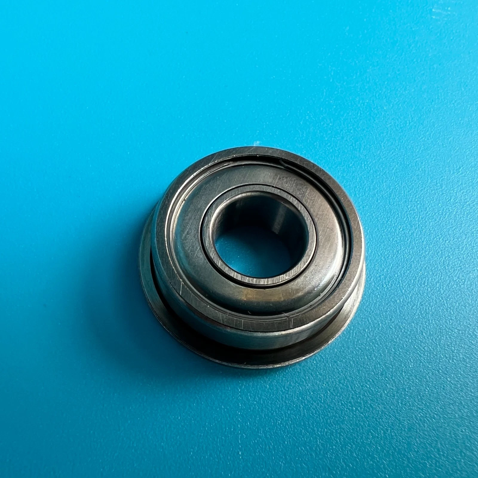 Metal bearing H001298 with smooth outer ring, black rubber O-ring, on a blue textured surface.