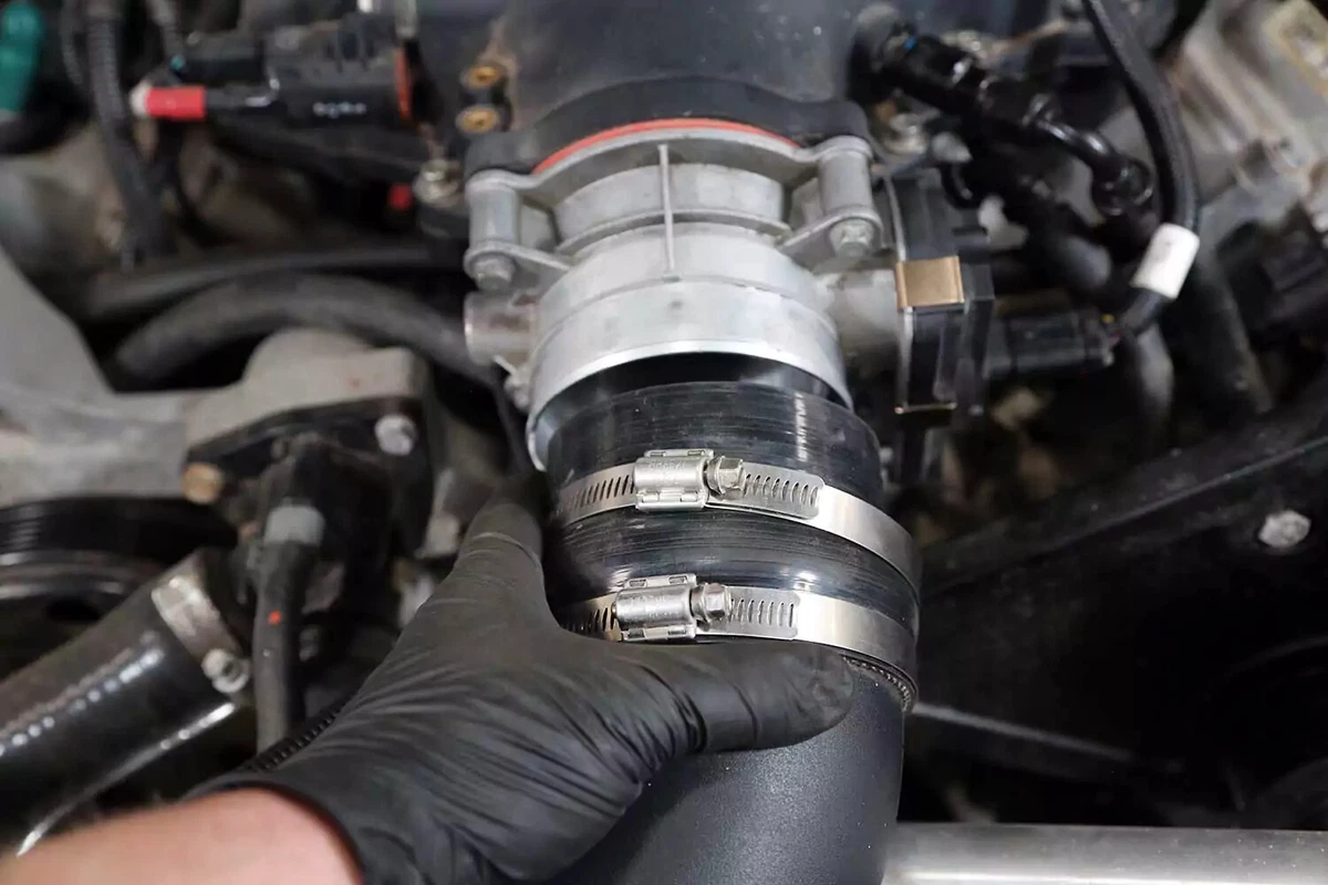 A mechanic slides the air intake tube off the throttle body.