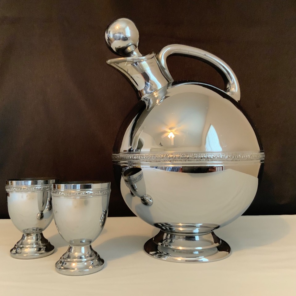 A chromium-plated spherical cocktail decanter with matching cups — it looks like a prop from a 1930s Hollywood film set.