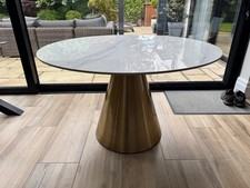 Dining table with round white marble effect ceramic top and gold base.