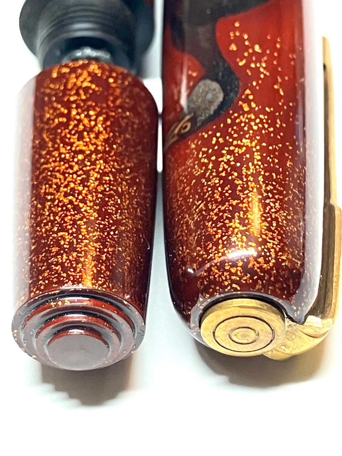 Close-up of orange HARUYAMA made ink shut off fountain pen with gold ring and black ink reservoir on white background.