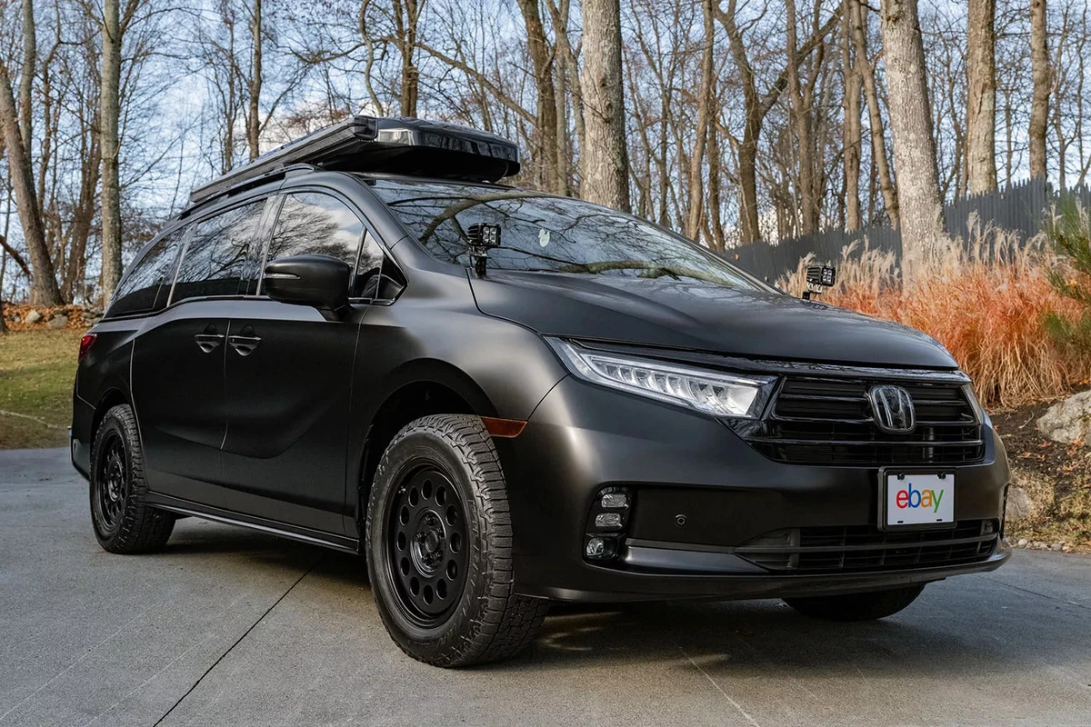 A black modified minivan with a rooftop carrier.