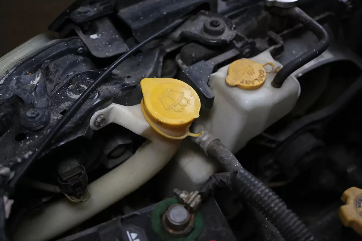 A vehicle's washer fluid reservoir with a yellow cap.