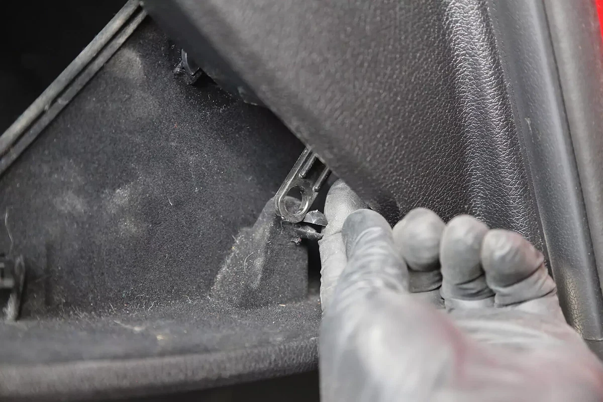 A mechanic wearing a black glove pops the lever of the stop holding the glove box into the dashboard.