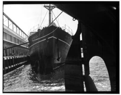 Ship docked in a harbor as viewed from underneath a large object C - Old Photo