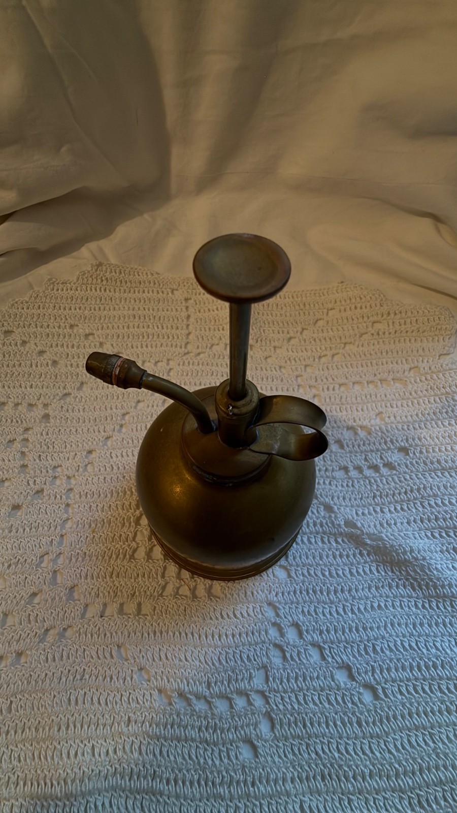 Vintage brass hand pump oiler with curved handle and long pump nozzle, made in USA on textured white fabric background.