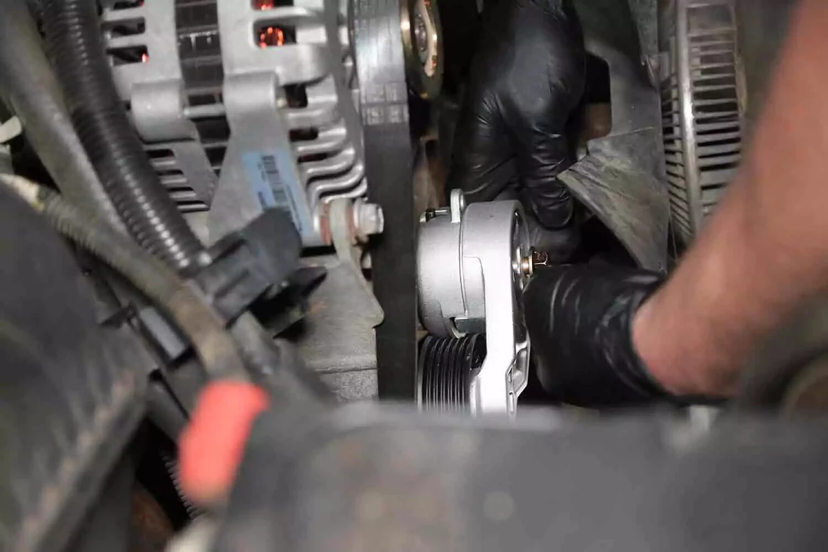 A mechanic wearing black glove places the new serpentine tensioner on the engine block.