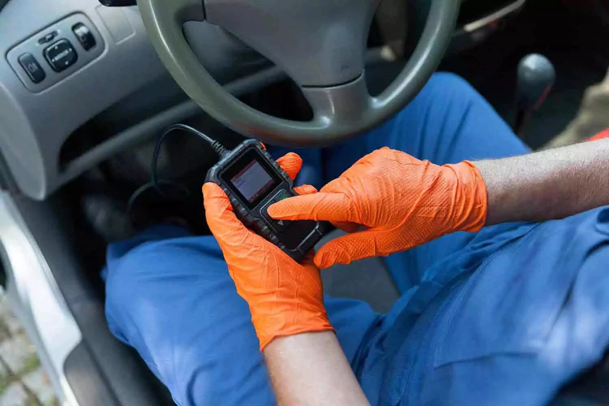 A mechanic wearing orange gloves, using a code reader plugged into the vehicle’s OBDII port.