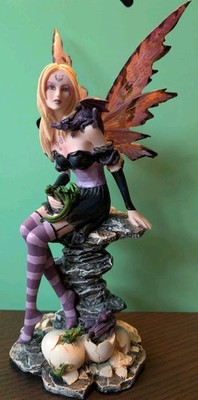Sitzende Fantasy Fee Figur mit Flügeln auf Felsen, Babydrachen