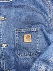 Blue denim Carhartt C59 chore coat with front pocket and brown Carhartt logo patch on left pocket.