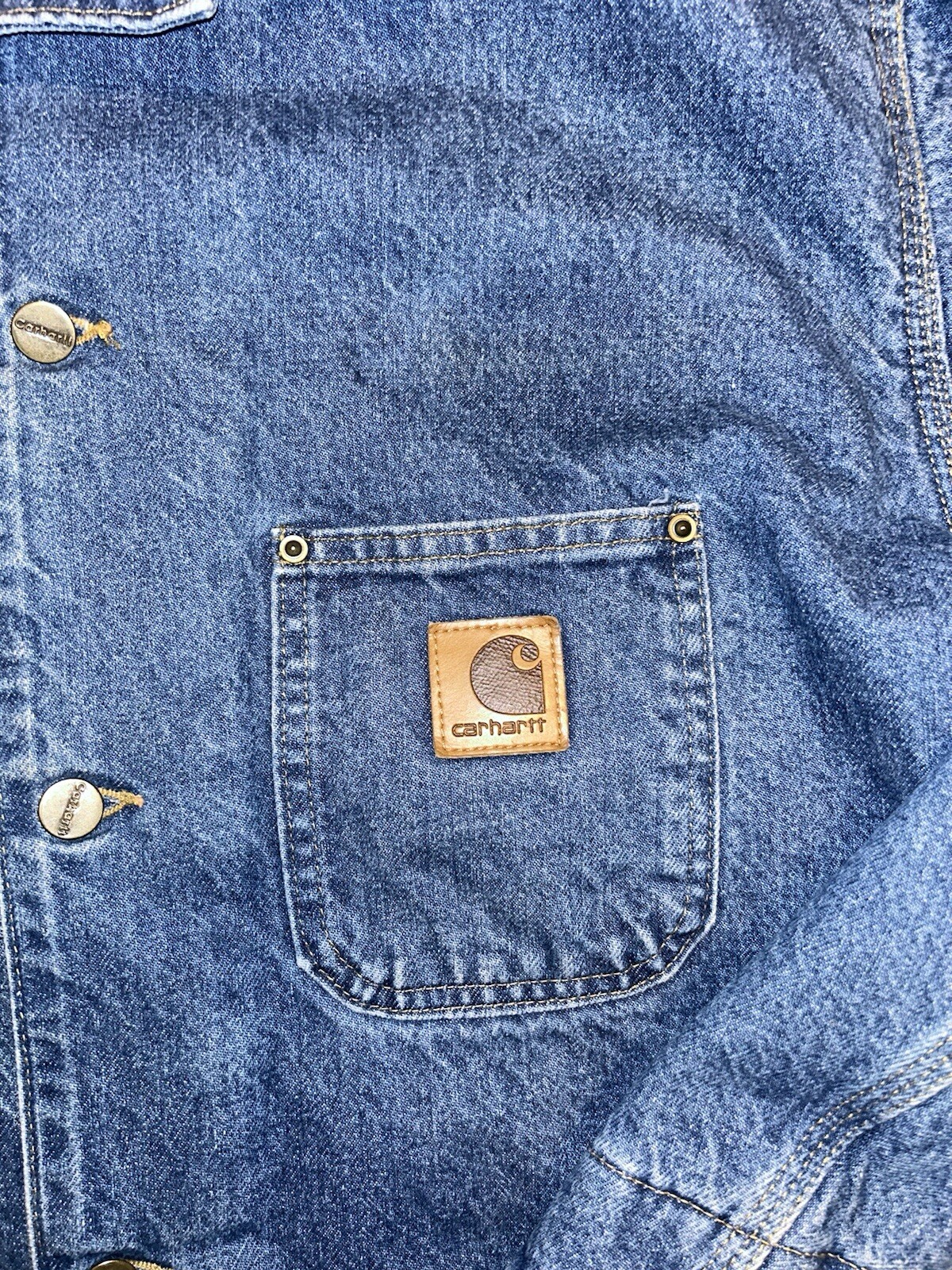 Blue denim Carhartt C59 chore coat with front pocket and brown Carhartt logo patch on left pocket.