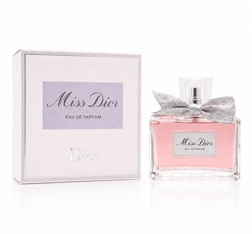 White Miss Dior Eau De Parfum spray bottle with pink cap and silver bow detail beside matching illustrated box.