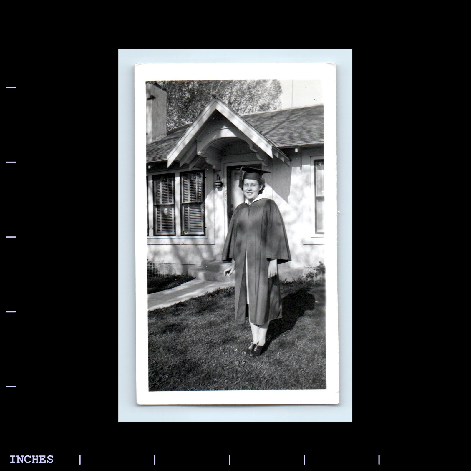 Vintage photo of woman in graduation cap and gown outside house