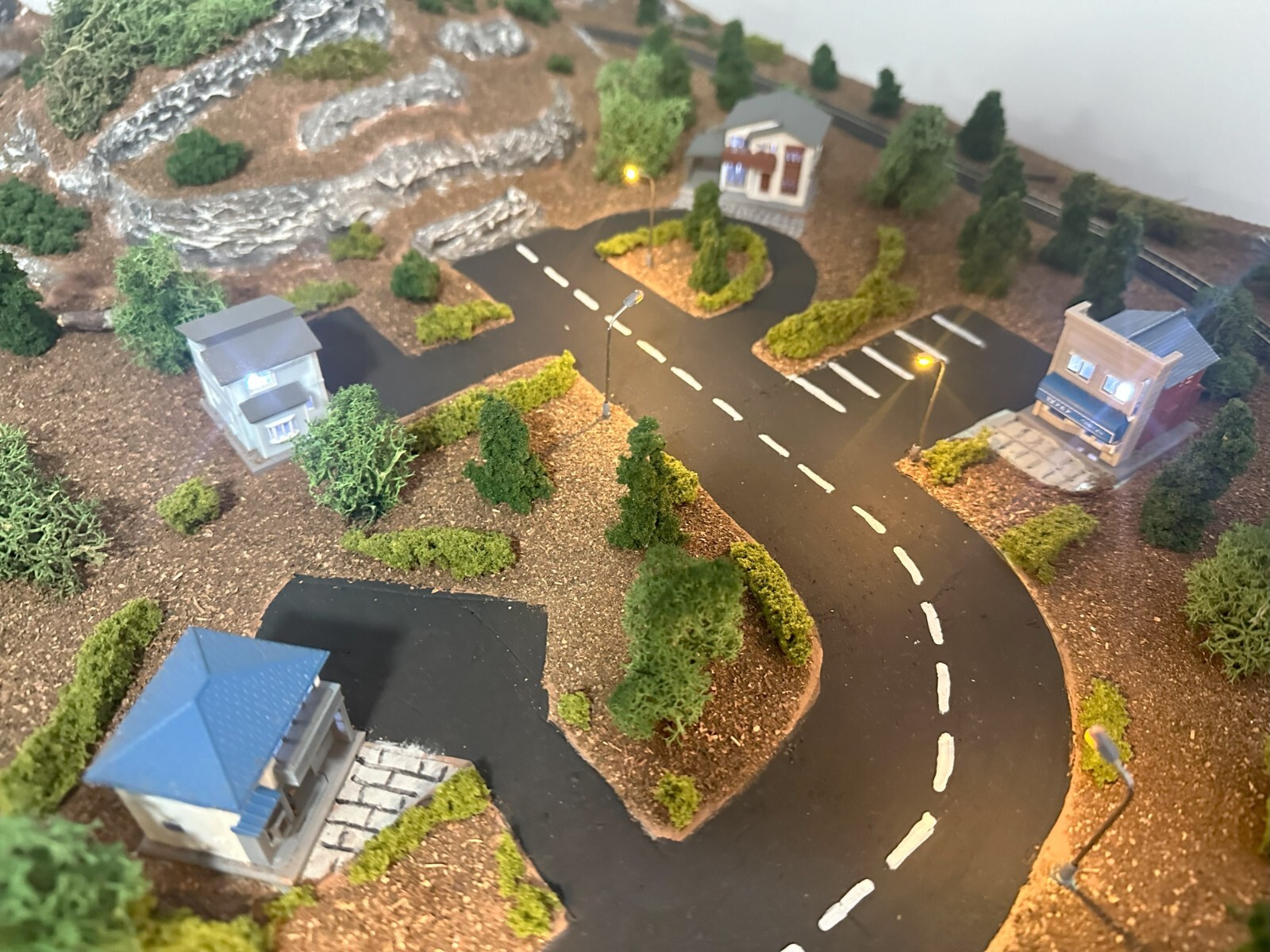 Z scale model town layout with curved road, buildings, trees, rocks, and lit street lamps.