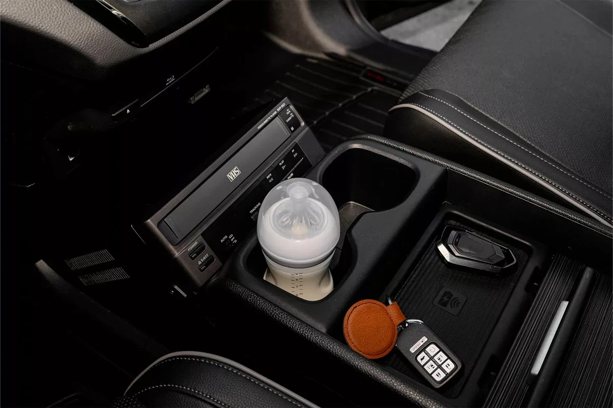 A baby bottle sitting in the center console of a modified minivan.