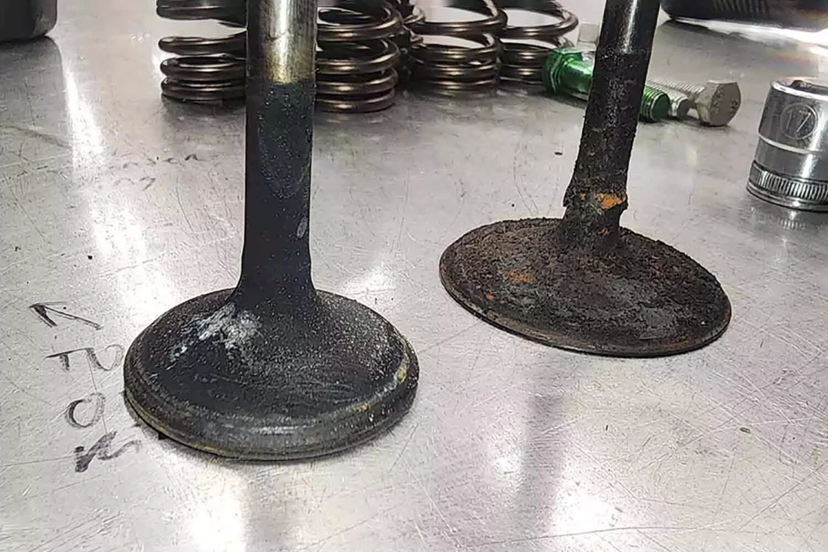 Two valves covered in carbon build-up, displayed on a metal work surface.