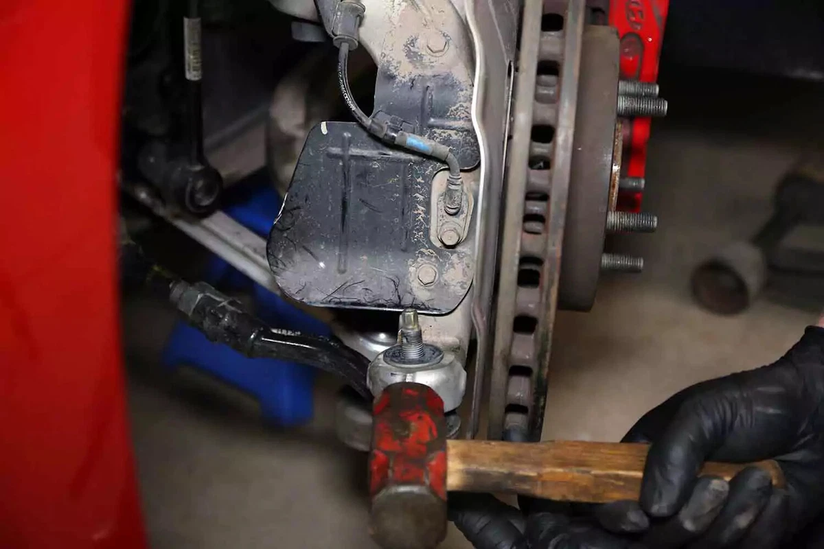 A mechanic taps the steering arm with a hammer to release the taper pin.