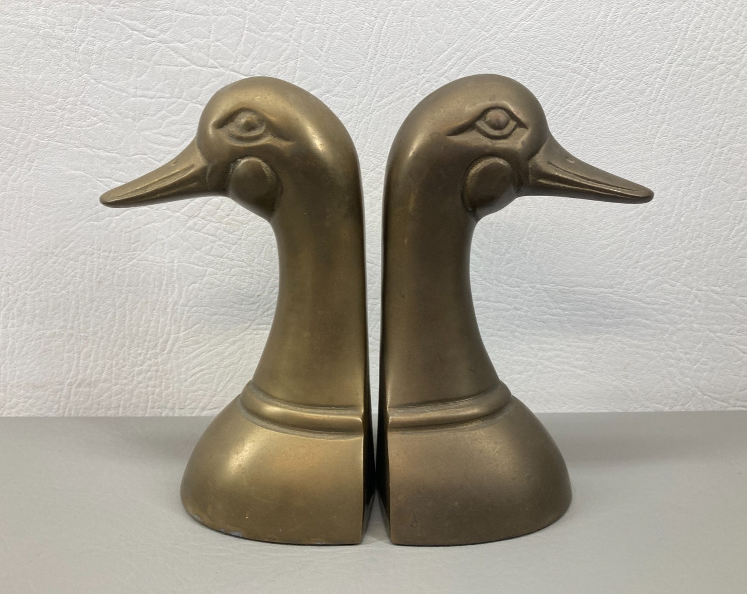 Pair of brass duck head bookends on a white background.