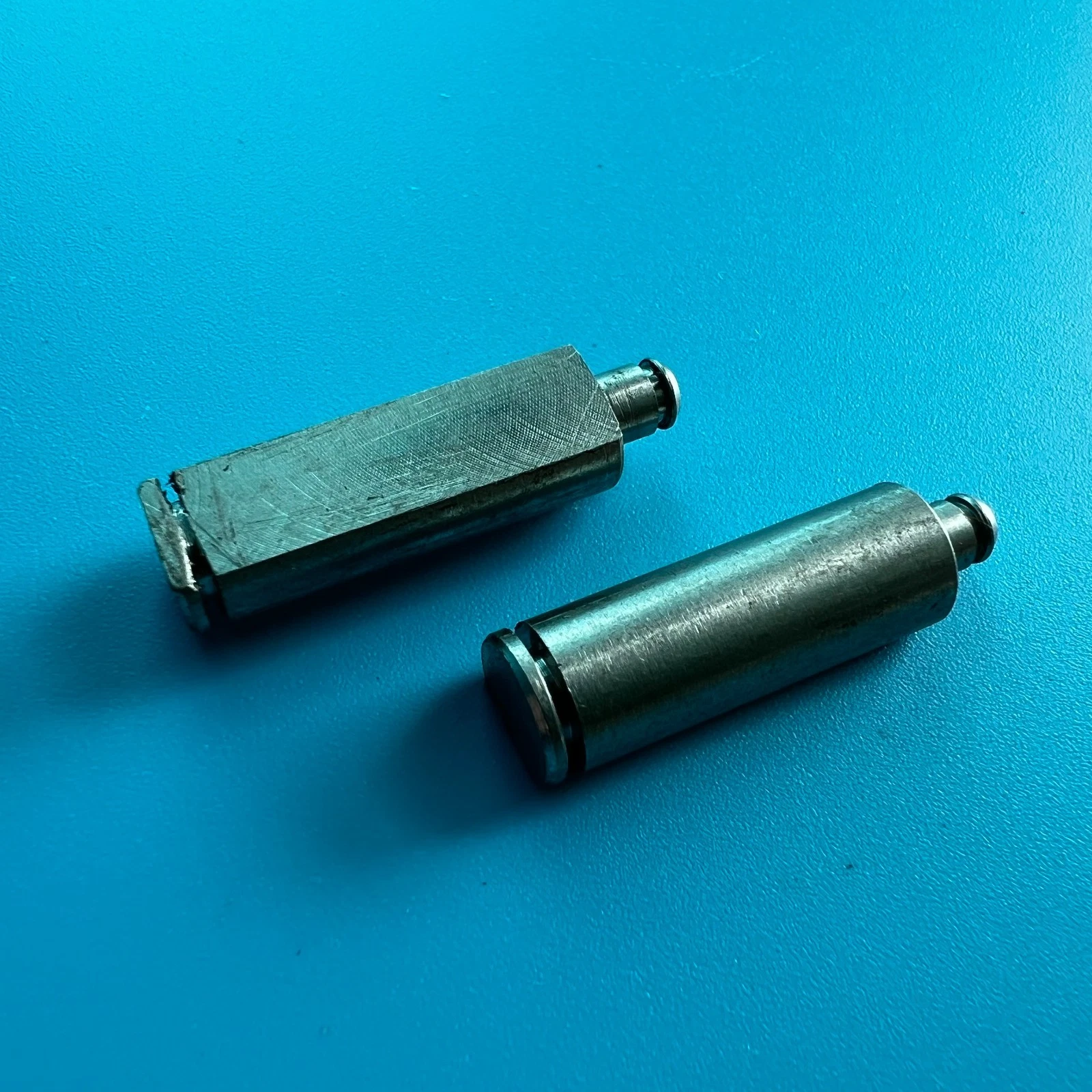 Two metal Fuji transport section shafts with threaded ends, displayed on a bright blue textured surface.