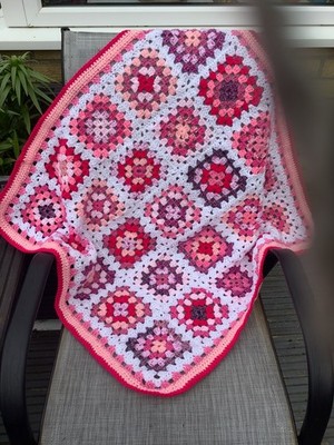 Handgefertigte gehäkelte afghanische Babydecke in leuchtenden und dezenten Rosatönen.